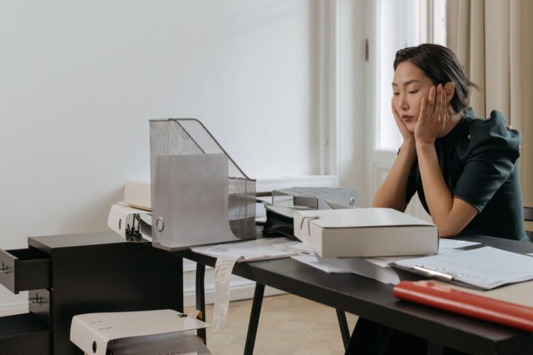 Tired professional resting her head on her hand at a busy desk